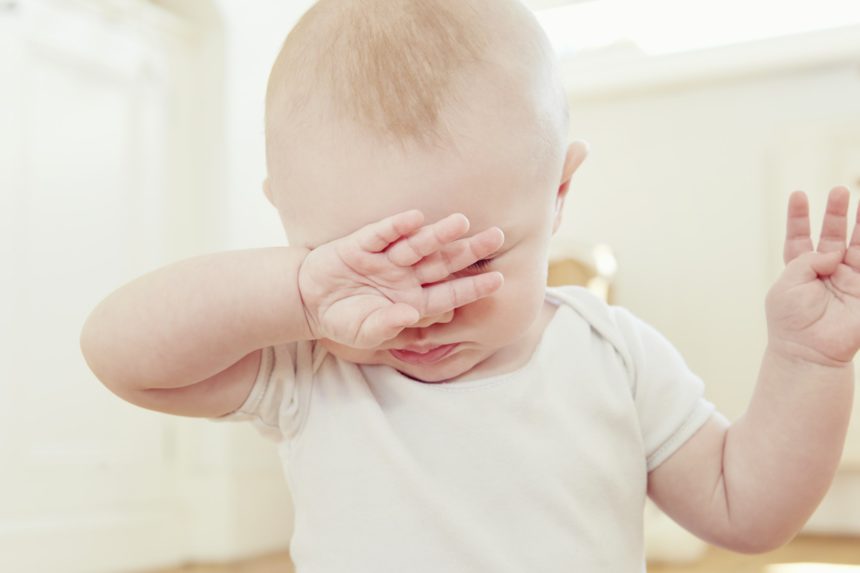 Close up of tired baby boy with hand covering eyes