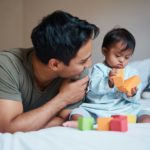 Father and down syndrome baby play education game with toys on bed for growth and happy together. M