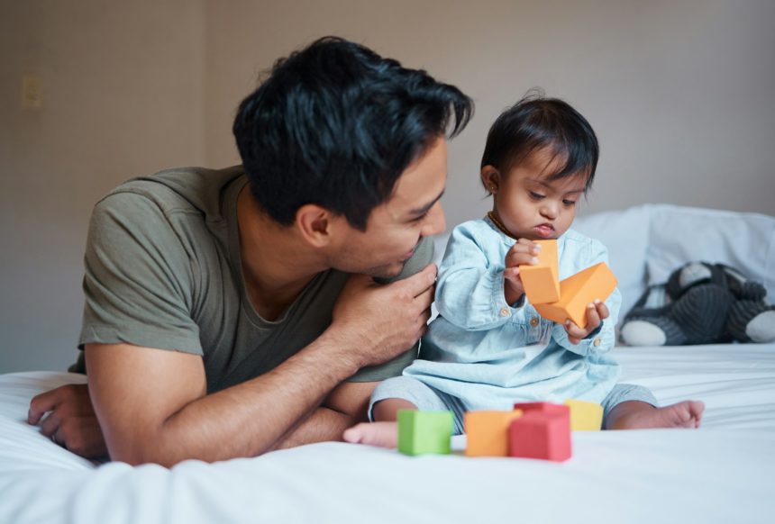 Father and down syndrome baby play education game with toys on bed for growth and happy together. M