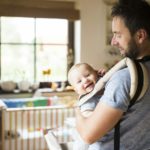 Happy father with baby in baby carrier at home