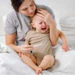 Mother taking temperature and comforting toddler. Baby crying because of fever.